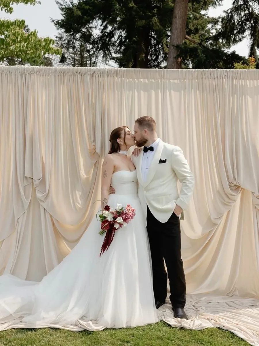 Novios besándose delante del fondo de tela color crema